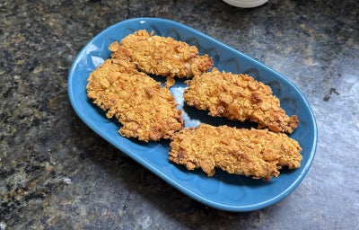 Fotografia mostra quatro filés de frango empanados, com textura crocante e dourada sobre um prato azul.