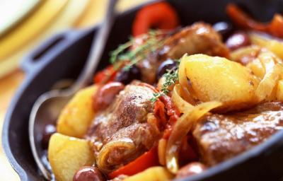 Fotografia em tons de vermelhos, em uma bancada de madeira de cor branca. Ao centro, um pano amarelo dobrado com um recipiente em cima contendo o bife e ao lado, há uma colher.
