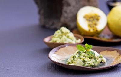 Foto da receita de salada de casca de maracujá, servida sobre um prato em formato de folha de árvore, numa bancada com um maracujá aberto ao fundo