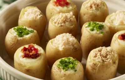 foto em tons de amarelo, verde e branco tirada de uma recipiente redondo branco com mini batatas recheadas. Abaixo um pano xadrez em tons de verde e branco. foto em tons de amarelo, verde e branco tirada de uma recipiente redondo branco com mini batatas recheadas. Abaixo um pano xadrez em tons de verde e branco.