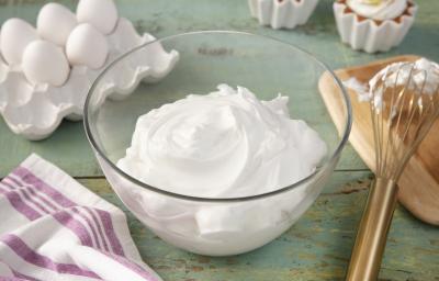 Fotografia em tons de verde em uma bancada de madeira verde, um pano branco com listras roxas, um recipiente de vidro com o merengue dentro dele. Ao fundo, potinhos com docinhos cobertos com merengue, ovos, tábua de madeira com um fouet. Fotografia em tons de verde em uma bancada de madeira verde, um pano branco com listras roxas, um recipiente de vidro com o merengue dentro dele. Ao fundo, potinhos com docinhos cobertos com merengue, ovos, tábua de madeira com um fouet.
