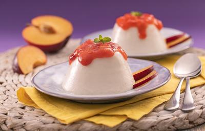 Foto em tons de roxo da receita de flan de ameixas frescas servidas em duas porções sobre pratos de porcelana lilás em cima de panos amarelos com colheres prateadas ao lado. Ao fundo e dentro dos pratos há fatias de ameixa fresca Foto em tons de roxo da receita de flan de ameixas frescas servidas em duas porções sobre pratos de porcelana lilás em cima de panos amarelos com colheres prateadas ao lado. Ao fundo e dentro dos pratos há fatias de ameixa fresca