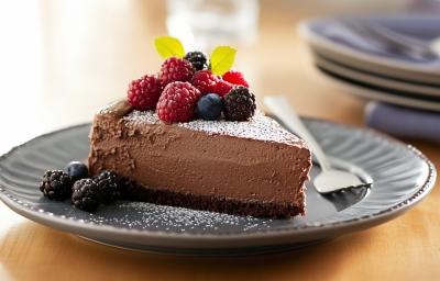 A foto mostra uma fatia da tortinha com uma base de biscoito de chocolate, recheada com creme de avelã e chocolate meio amargo. O topo da torta é coberto por frutas vermelhas frescas, como morangos, amoras e framboesas. A foto mostra uma fatia da tortinha com uma base de biscoito de chocolate, recheada com creme de avelã e chocolate meio amargo. O topo da torta é coberto por frutas vermelhas frescas, como morangos, amoras e framboesas.