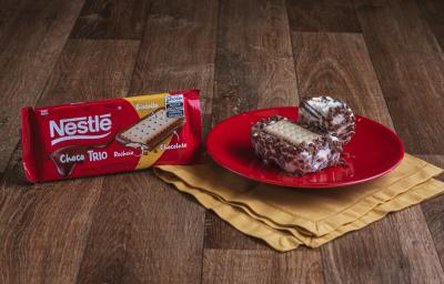 Foto da Receita de Sanduíche de Sorvete com Choco Trio. Observa-se dois sanduíches (um inteiro e um mordido) sobre um prato vermelho redondo e pequeno e, ao lado, a embalagem de ChocoTrio Foto da Receita de Sanduíche de Sorvete com Choco Trio. Observa-se dois sanduíches (um inteiro e um mordido) sobre um prato vermelho redondo e pequeno e, ao lado, a embalagem de ChocoTrio
