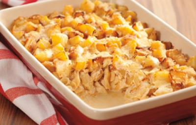 Fotografia em tons de vermelho e amarelo de uma bancada de madeira com um pano quadriculado branco e vermelho, uma travessa retangular vermelha por fora e bege por dentro com o bacalhau gratinado com cubos de batata por cima, faltando uma porção.