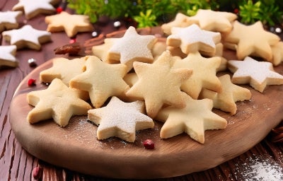 Em cima de uma mesa, prato com biscoitos em formato de estrelas, polvilhados com açúcar de confeiteiro.