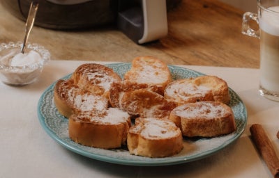 Prato azul com fatias de rabanada polvilhadas com açúcar e canela e uma air fryer no fundo.