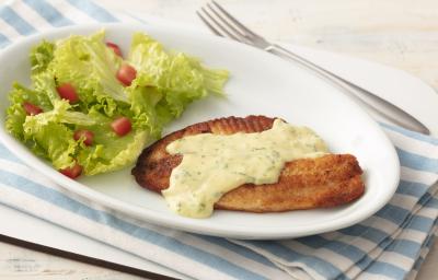 Fotografia em tons de azul em uma bancada de madeira clara com um pano listrado azul claro e um prato oval branco com o filé de pescada com molho de limão e mostrada e salada de alface com tomates. Fotografia em tons de azul em uma bancada de madeira clara com um pano listrado azul claro e um prato oval branco com o filé de pescada com molho de limão e mostrada e salada de alface com tomates.
