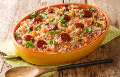 Fotografia mostra um arroz com pedaços de linguiça e temperos verdes dentro de uma travessa de servir. Fotografia mostra um arroz com pedaços de linguiça e temperos verdes dentro de uma travessa de servir.