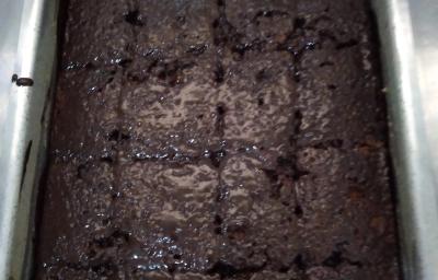Fotografia de uma forma retangular de alumínio grande com um bolo e calda de chocolate com granulado.