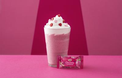 Foto da receita de Frappé. Observa-se um fundo rosa com um copo alto decorado de chantily e confeitos de coração com um kit kat de morango na frente. Foto da receita de Frappé. Observa-se um fundo rosa com um copo alto decorado de chantily e confeitos de coração com um kit kat de morango na frente.