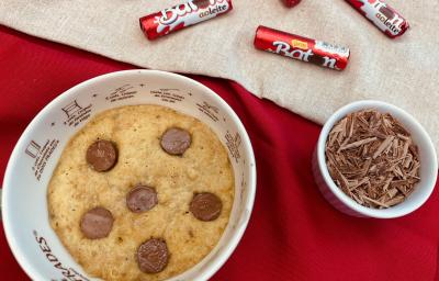Fotografia em tons de vermelho com um recipiente ao centro. Dentro do recipiente existe um cookie com pedaços de chocolate BATON. Ao lado existe um pequeno pote com raspas de chocolate e ao fundo existe algumas embalagens de chocolate BATON Fotografia em tons de vermelho com um recipiente ao centro. Dentro do recipiente existe um cookie com pedaços de chocolate BATON. Ao lado existe um pequeno pote com raspas de chocolate e ao fundo existe algumas embalagens de chocolate BATON