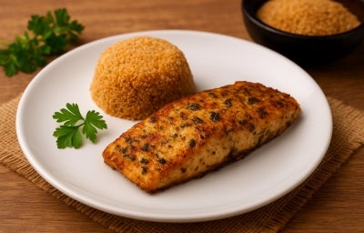 Fotografia de um filé de peixe com chibé e três folhas de salsinha em um prato branco e raso. Ao fundo tem mais folhas de salsinha e chibé em um recipiente preto e fundo pequeno. Fotografia de um filé de peixe com chibé e três folhas de salsinha em um prato branco e raso. Ao fundo tem mais folhas de salsinha e chibé em um recipiente preto e fundo pequeno.