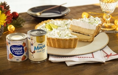 Imagem de uma torta de limão em um prato e uma fatia na espátula. Ao lado, uma lata de Creme de Leite Nestlé e Leite Moça.
