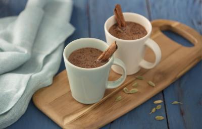 Fotografia em tons de azul em uma bancada de madeira azul, um pano azul, uma tábua de madeira com duas xícaras brancas com o chocolate quente com canela dentro delas. Fotografia em tons de azul em uma bancada de madeira azul, um pano azul, uma tábua de madeira com duas xícaras brancas com o chocolate quente com canela dentro delas.