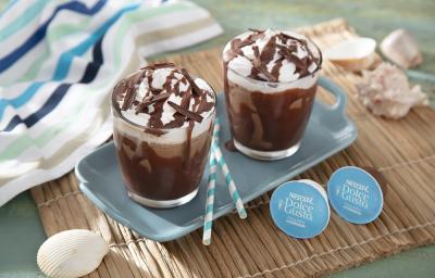 Foto da receita de frapê mocha servida em duas xícaras de vidro em cima de uma base de porcelana azul clara sobre uma esteira de madeira com cápsulas de dolce gusto frapê ao lado Foto da receita de frapê mocha servida em duas xícaras de vidro em cima de uma base de porcelana azul clara sobre uma esteira de madeira com cápsulas de dolce gusto frapê ao lado