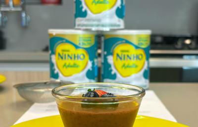 Fotografia em tons de amarelo com um potinho de vidro ao centro. Dentro do pote existe uma receita de mousse de chocolate com Ninho Adulto e chia Fotografia em tons de amarelo com um potinho de vidro ao centro. Dentro do pote existe uma receita de mousse de chocolate com Ninho Adulto e chia