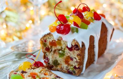 Fotografia de um bolo frutado de natal com calda e frutas secas e cristalizadas, o bolo foi feito na forma de bolo inglês, sobre um apoio de vidro branco, com luzes de natal ao fundo. Fotografia de um bolo frutado de natal com calda e frutas secas e cristalizadas, o bolo foi feito na forma de bolo inglês, sobre um apoio de vidro branco, com luzes de natal ao fundo.