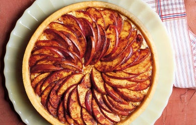 Foto tirada de cima de uma torta redonda de maça em cima de um prato branco. A torta é decorada por várias maças cortadas.