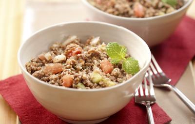 Fotografia em tons de vermelho em uma mesa de madeira clara com uma tábua de madeira, dois guardanapos de papel vermelhos e dois recipientes redondos com a salada de trigo com carne moída. Fotografia em tons de vermelho em uma mesa de madeira clara com uma tábua de madeira, dois guardanapos de papel vermelhos e dois recipientes redondos com a salada de trigo com carne moída.