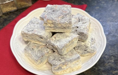 Foto aproximada da receita de Palha Italiana Dois Amores, servida em pedaços um sobre o outro, em um prato branco numa bancada de mármore com um tecido vermelho