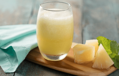 Fotografia em tons de verde em uma bancada de madeira mesclada, um pano verde água, uma tábua de madeira, um copo de vidro com a vitamina de abacaxi dentro, folhas de hortelã e pedaços de abacaxi ao lado. Fotografia em tons de verde em uma bancada de madeira mesclada, um pano verde água, uma tábua de madeira, um copo de vidro com a vitamina de abacaxi dentro, folhas de hortelã e pedaços de abacaxi ao lado.
