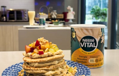 Fotografia em tons de azul e amarelo em uma bancada de cozinha com um prato azul ao centro e panquecas com creme e frutas em cima.