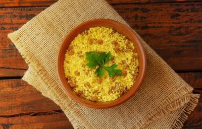 fotografia em tons de marrom e amarelo de uma bancada marrom vista de cima. Contém um pano bege e por cima um recipiente redondo marrom com farofa e pedaços de bacon. fotografia em tons de marrom e amarelo de uma bancada marrom vista de cima. Contém um pano bege e por cima um recipiente redondo marrom com farofa e pedaços de bacon.