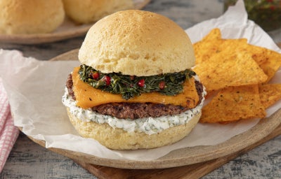 imagem mostra um hambúrguer montado com pão de queijo, recheio de carne, queijo, vinagrete, couve crispy e requeijão cremoso.