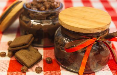 Foto de uma bancada forrada com uma toalha quadriculada vermelha e branca. Sobre ela há 2 potes de vidros com a receita de Brownie de Nescau com Brigadeiro. Um deles está fechado e o outro aberto. Além disso há 2 biscoitos e algumas bolinhas de cereal Foto de uma bancada forrada com uma toalha quadriculada vermelha e branca. Sobre ela há 2 potes de vidros com a receita de Brownie de Nescau com Brigadeiro. Um deles está fechado e o outro aberto. Além disso há 2 biscoitos e algumas bolinhas de cereal