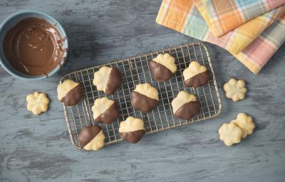 fotografia vista de cima de uma bancada cinza, contém uma grade e por cima docinhos de leite MOÇA com chocolate. Ao lado um recipiente redondo e azul com chocolate dentro e um pano em tons de amarelo, laranja, azul e rosa fotografia vista de cima de uma bancada cinza, contém uma grade e por cima docinhos de leite MOÇA com chocolate. Ao lado um recipiente redondo e azul com chocolate dentro e um pano em tons de amarelo, laranja, azul e rosa