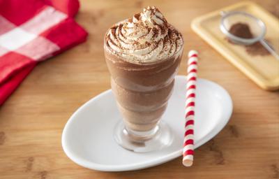 Foto da receita de Milkshake de Cappuccino. Observa-se um copo alto com a bebida decorado com chantilly e polvilhado de chocolate em pó. Ao lado direito, um canudo vermelho e branco para decorar. Foto da receita de Milkshake de Cappuccino. Observa-se um copo alto com a bebida decorado com chantilly e polvilhado de chocolate em pó. Ao lado direito, um canudo vermelho e branco para decorar.