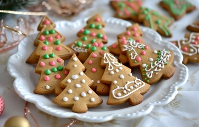 Em cima de uma mesa, prato redondo com biscoitos em formato de árvore de Natal, decorados com glacê branco, verde e rosa. Em cima de uma mesa, prato redondo com biscoitos em formato de árvore de Natal, decorados com glacê branco, verde e rosa.