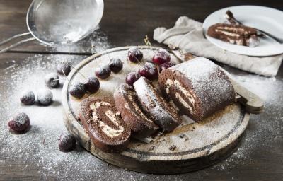Fotografia de um rocambole de pão-de-ló de chocolate, recheado com Leite MOÇA, coco e castanha-de-caju. Por cima tem um povilhado de açúcar de confeiteiro Fotografia de um rocambole de pão-de-ló de chocolate, recheado com Leite MOÇA, coco e castanha-de-caju. Por cima tem um povilhado de açúcar de confeiteiro