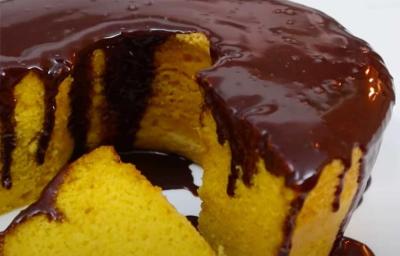 Foto da receita de Bolo de Cenoura com Cobertura de Chocolate. Observa-se um bolo com furo no meio bem de perto com uma fatia cortada e a cobertura de chocolate escorrendo Foto da receita de Bolo de Cenoura com Cobertura de Chocolate. Observa-se um bolo com furo no meio bem de perto com uma fatia cortada e a cobertura de chocolate escorrendo