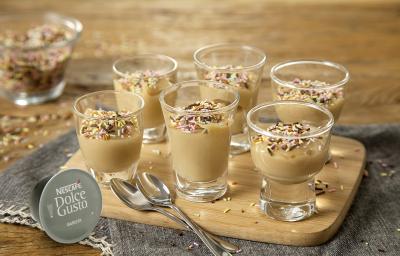 Foto de uma mesa com um pano cinza e uma tábua de madeira em cima, com 6 potinhos de vidro com brigadeiro dentro e decorados com granulado Foto de uma mesa com um pano cinza e uma tábua de madeira em cima, com 6 potinhos de vidro com brigadeiro dentro e decorados com granulado