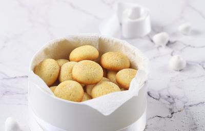 Fotografia em tons de branco de alguns biscoitos de massa branca dentro de uma cestinha branca com uma fita também branca amarrando-a. Ao fundo, alguns suspiros e um biscoito quebrado ao meio, sobre uma mesa de mármore branca. Fotografia em tons de branco de alguns biscoitos de massa branca dentro de uma cestinha branca com uma fita também branca amarrando-a. Ao fundo, alguns suspiros e um biscoito quebrado ao meio, sobre uma mesa de mármore branca.
