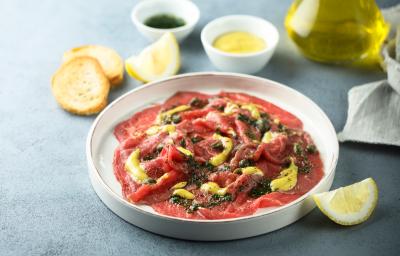 Foto da receita de Carpaccio com Alcaparras e Molho de Mostarda. Observa-se um prato branco grande com a carne fina dentro em rodelas, com molho e alcaparras. Foto da receita de Carpaccio com Alcaparras e Molho de Mostarda. Observa-se um prato branco grande com a carne fina dentro em rodelas, com molho e alcaparras.