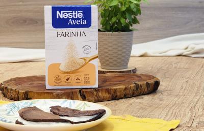 Fotografia em tons de marrom com um prato redondo ao centro. Em cima do prato existe duas panquecas de chocolate com aveia recheadas com um creme de iogurte. Ao fundo existe uma embalagem de Farinha de aveia NESTLÉ Fotografia em tons de marrom com um prato redondo ao centro. Em cima do prato existe duas panquecas de chocolate com aveia recheadas com um creme de iogurte. Ao fundo existe uma embalagem de Farinha de aveia NESTLÉ