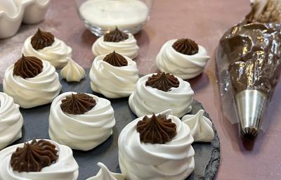 Foto da receita de vol au vent servida em diversas porções sobre uma base de porcelana cinza escura em cima de uma mesa em tons de cor de rosa. Ao fundo há um copo de vidro com creme de leite e um saco com bico de confeitar com chocolate Foto da receita de vol au vent servida em diversas porções sobre uma base de porcelana cinza escura em cima de uma mesa em tons de cor de rosa. Ao fundo há um copo de vidro com creme de leite e um saco com bico de confeitar com chocolate