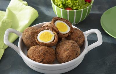 Foto da receita de Bolovo. Observa-se um recipiente com 6 bolovos, sendo que um está cortado no meio. Atrás, um recipiente com salada decora.