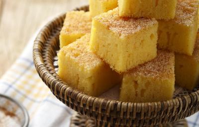 Foto de pedaços quadrados de bolo de fubá em um recipiente marrom em cima de um pano branco com detalhes laranja e azul Foto de pedaços quadrados de bolo de fubá em um recipiente marrom em cima de um pano branco com detalhes laranja e azul