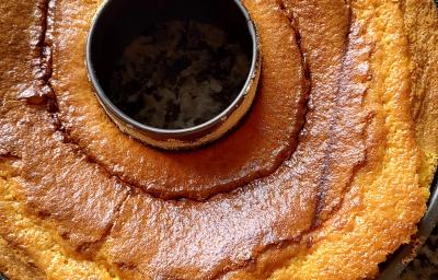 Fotografia de uma forma de bolo preta com furo central com um bolo de cenoura brilhante sobre uma bancada.