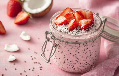 Imagem mostra um recipiente de vidro com um creme branco com pontinhos escuros, pedaços de coco e morango