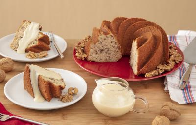 Foto da Receita de Bolo de Nozes com Molho doce. Observa-se dois pratos de sobremesa com pedaços do bolo e a calda. Ao lado direito, um prato redondo vermelho grande com o restante do bolo, decorado por nozes. Foto da Receita de Bolo de Nozes com Molho doce. Observa-se dois pratos de sobremesa com pedaços do bolo e a calda. Ao lado direito, um prato redondo vermelho grande com o restante do bolo, decorado por nozes.