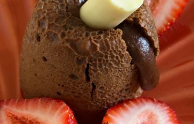 Fotografia de um petit gateau de chocolate com baton duo em um prato vermelho fundo com morangos.