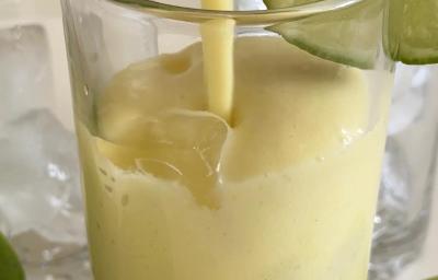 Fotografia em tons claros de um copo de vidro com limonada alemã, com gelos e uma fatia de limão decorando o copo. Fotografia em tons claros de um copo de vidro com limonada alemã, com gelos e uma fatia de limão decorando o copo.