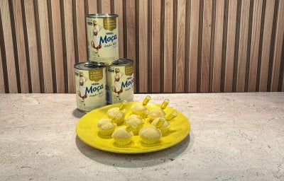 Docinhos cobertos com coco ralado em forminhas amarelas, servidos em prato amarelo com Leite Moça ao fundo.