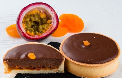 Fotografia de duas minitortinhas de maracujá com chocolate sobre um apoio pequeno preto quadrado.