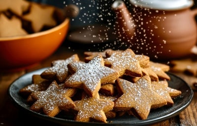 Em cima de uma mesa, prato redondo preto com biscoitos em formato de estrelas, polvilhado com açúcar de confeiteiro. Em cima de uma mesa, prato redondo preto com biscoitos em formato de estrelas, polvilhado com açúcar de confeiteiro.